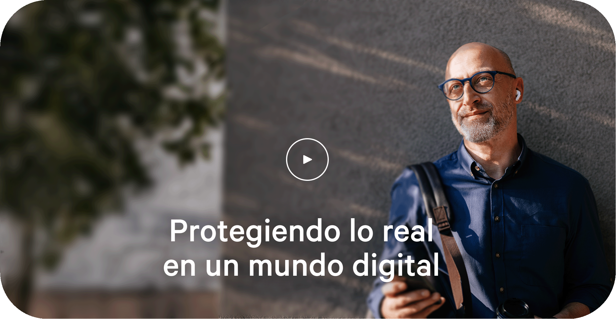 Hombre apoyado contra una pared exterior con un dispositivo móvil en la mano